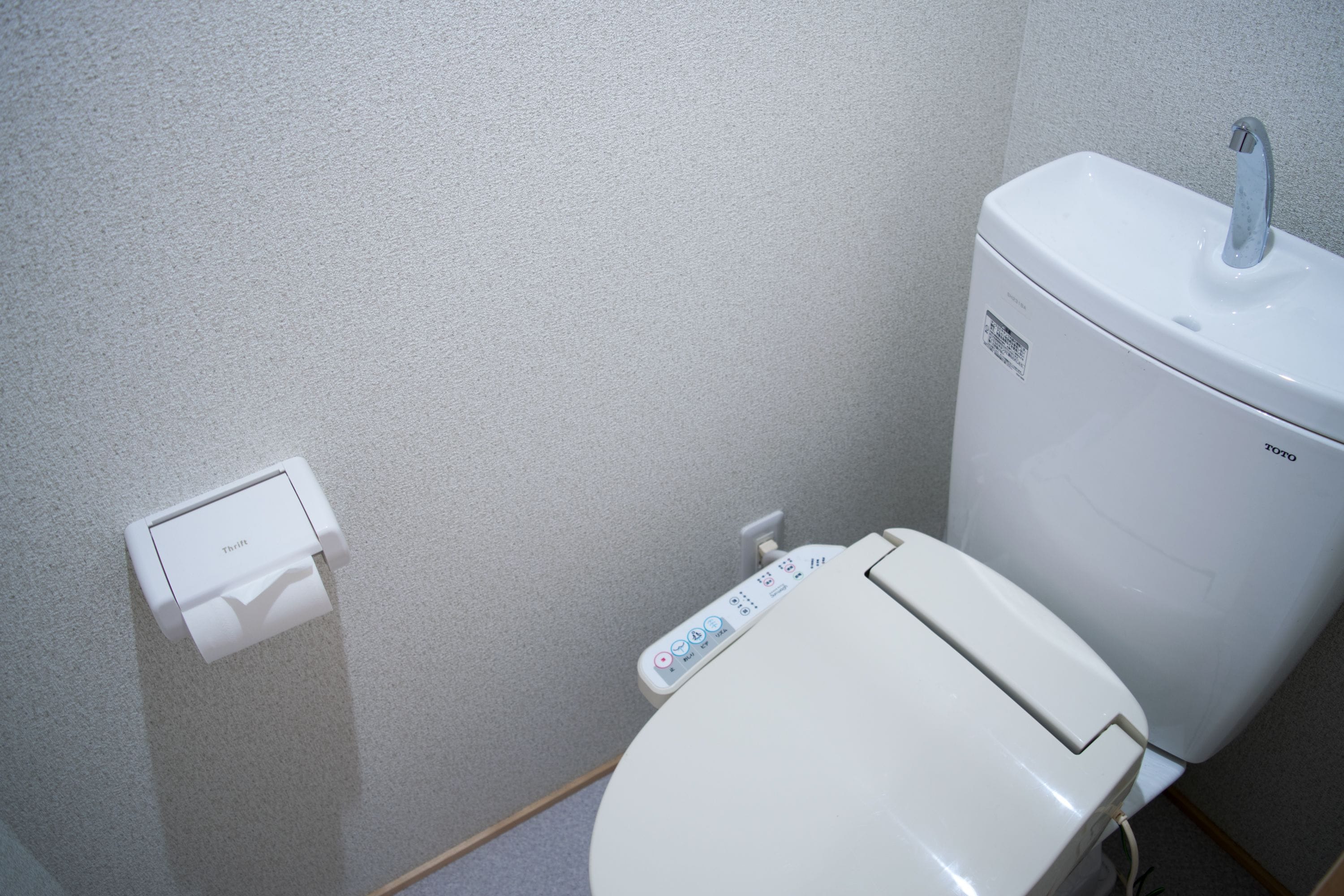 A modern toilet with a control panel and a wall-mounted flush button.