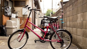 Una bicicleta rosa estacionada junto a una pared con una moto.