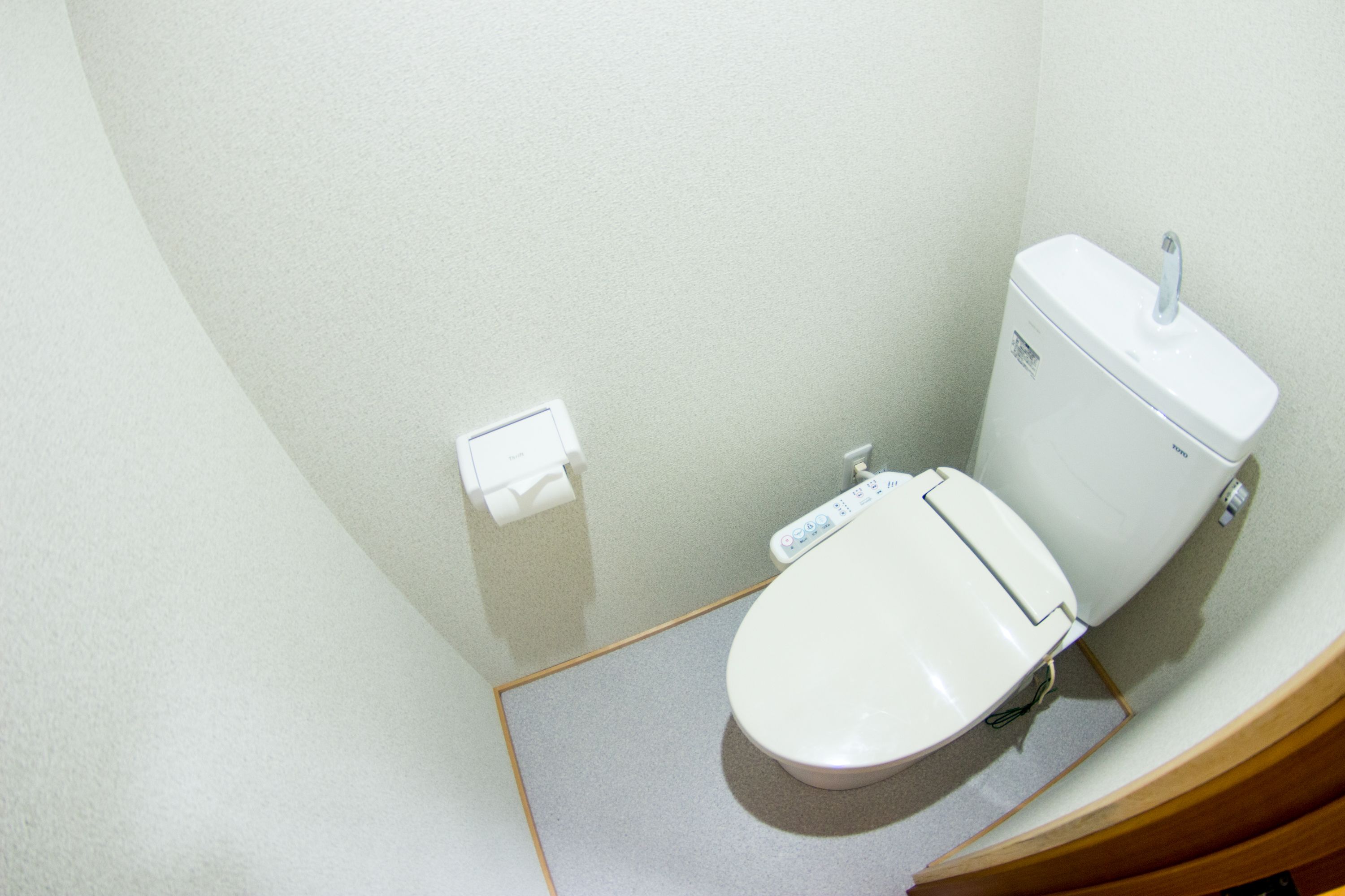 Een kleine, moderne badkamer met een wit toilet, een papieren handdoekdispenser en een bedieningsknop voor de spoeling op de muur.
