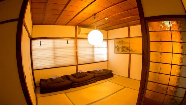 Una habitación japonesa tradicional con suelo de tatami, una mesa baja con cojines y una puerta corredera.