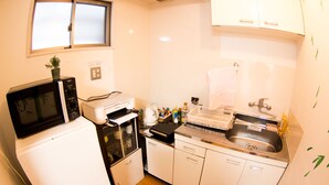 Cocina compacta con microondas, horno y lavaplatos. Hay un ventanal sobre el lavaplatos y una planta encima del microondas.