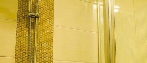 Ducha con pared texturizada, cabezal de ducha de mano y dispensador de jabón.
