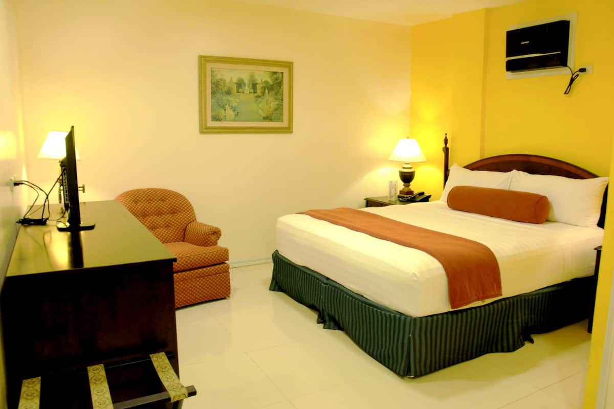Une chambre d’hôtel avec un lit, un bureau, une chaise et deux lampes.