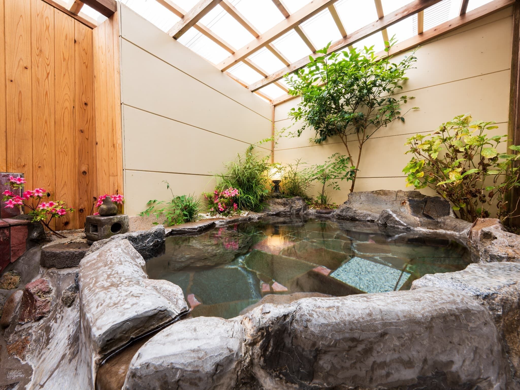 Un jardin intérieur paisible, avec un petit étang, des poutres en bois et diverses plantes.