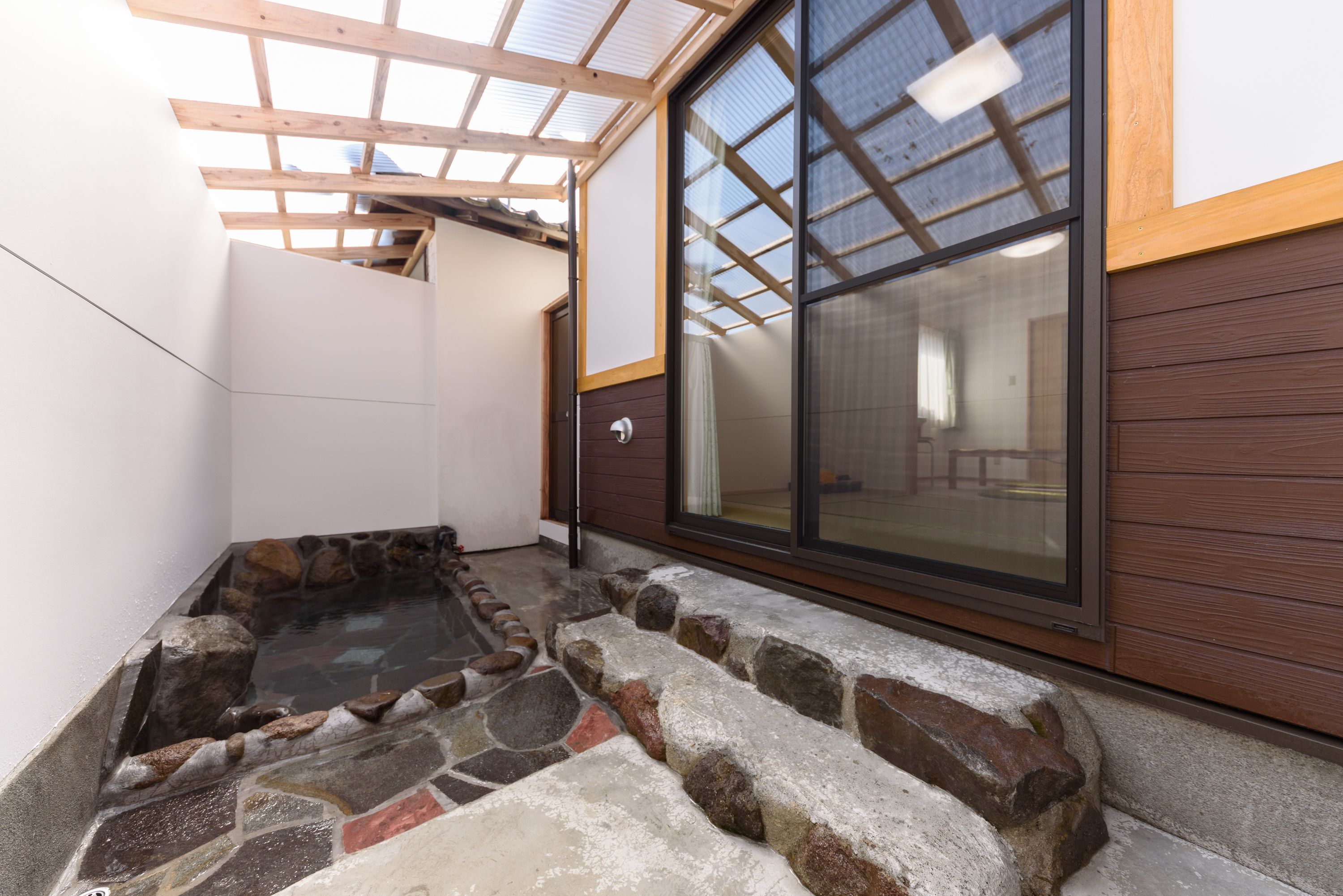 A spa area with a stone hot tub, wooden deck, and a large sliding glass door leading to an indoor space.