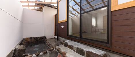 A spa area with a stone hot tub, wooden deck, and a large sliding glass door leading to an indoor space.