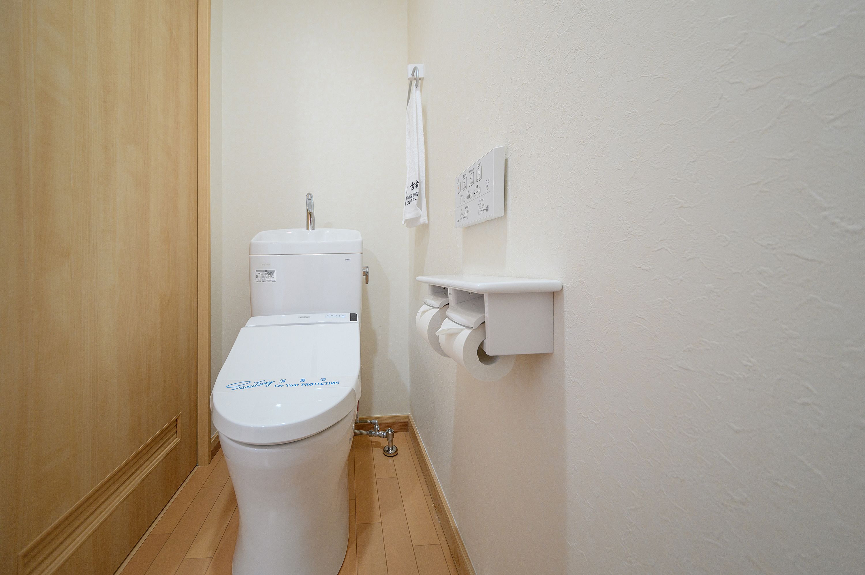 A small, clean bathroom with a toilet, a white towel hanging on a rack, and a toilet paper holder.