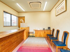 A reception area with a wooden counter, a small desk with a telephone, and a row of blue chairs.