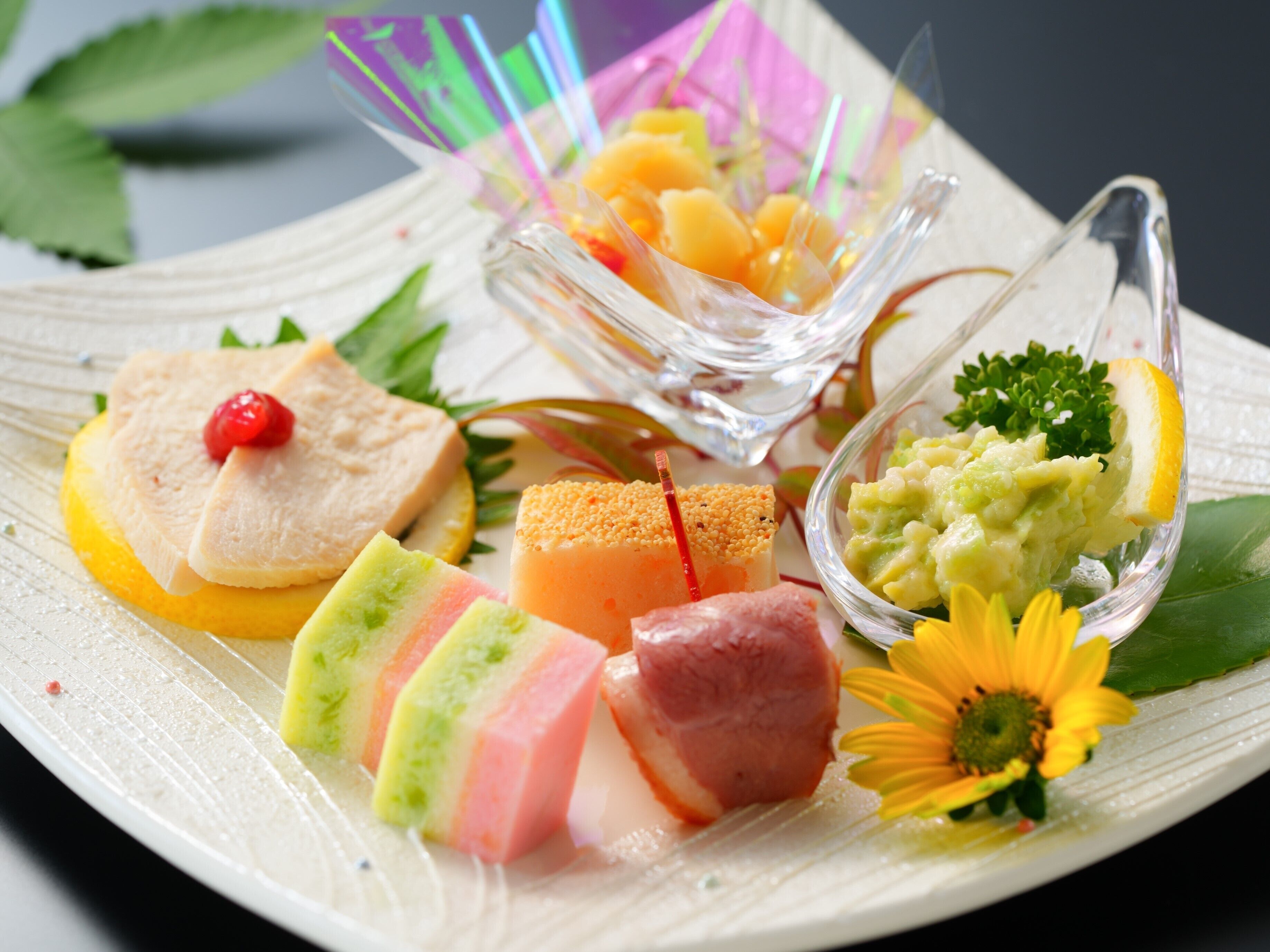 A variety of colorful food items arranged on a plate, including slices of cake, a piece of fish, and a bowl of fruit.