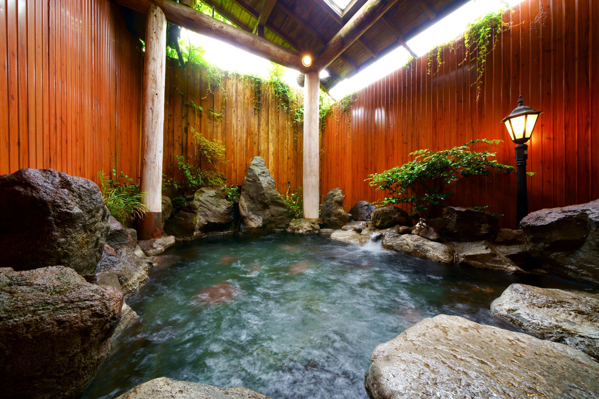 A hot spring area with wooden walls, rocks, and a lantern.