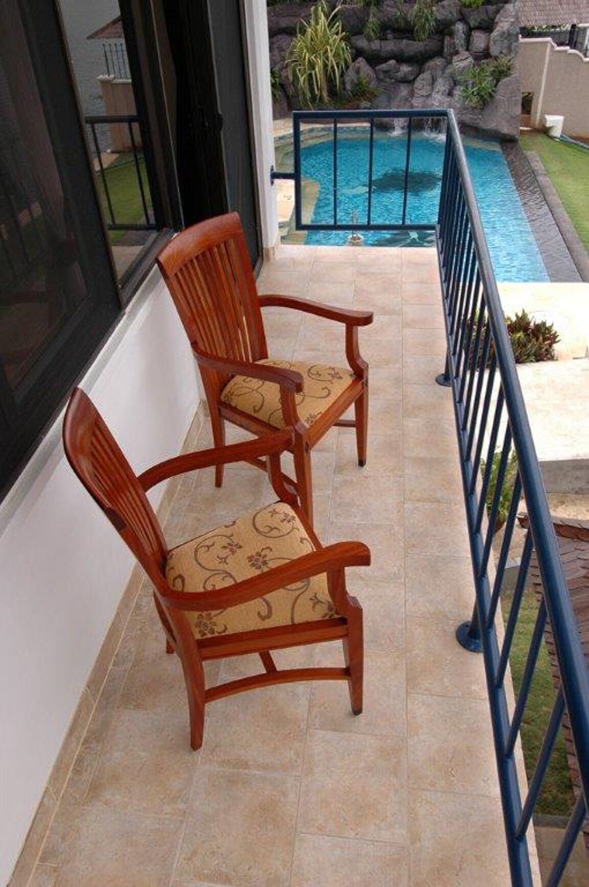 A balcony with two wooden chairs and a pool in the background.