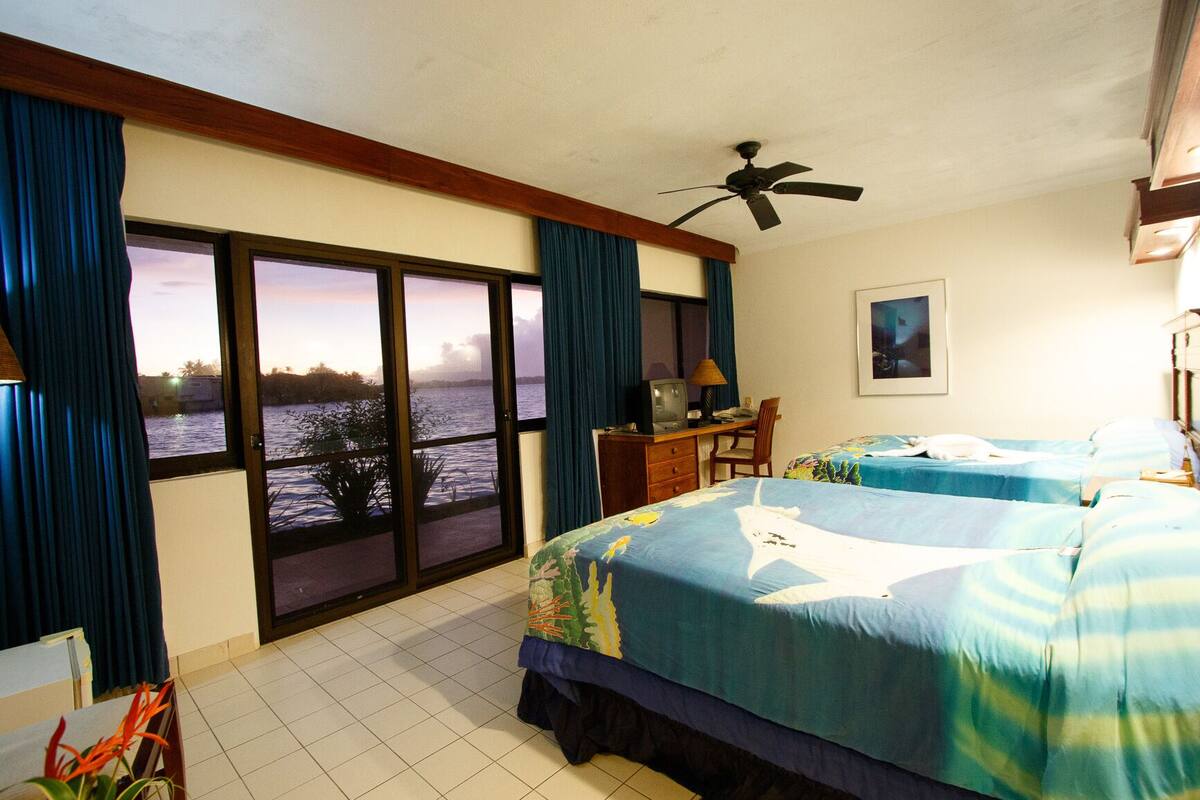 A hotel room with two beds, a desk, a television, and a view of the water.