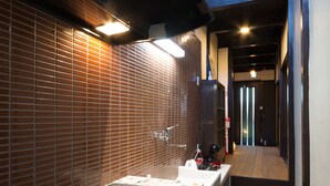 Un couloir étroit avec un mur recouvert de carreaux, un petit lavabo et une paire de chaussures posées sur le sol.