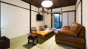 Une pièce de style japonais traditionnel, avec un sol recouvert de tatamis, une table basse, un canapé et un téléviseur fixé au mur.