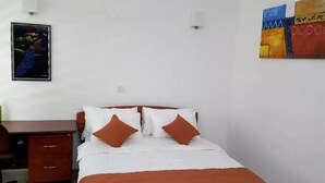 Een hotelkamer met een bed, een bureau en een stoel. Er hangt een schilderij aan de muur en een lamp boven het bed.