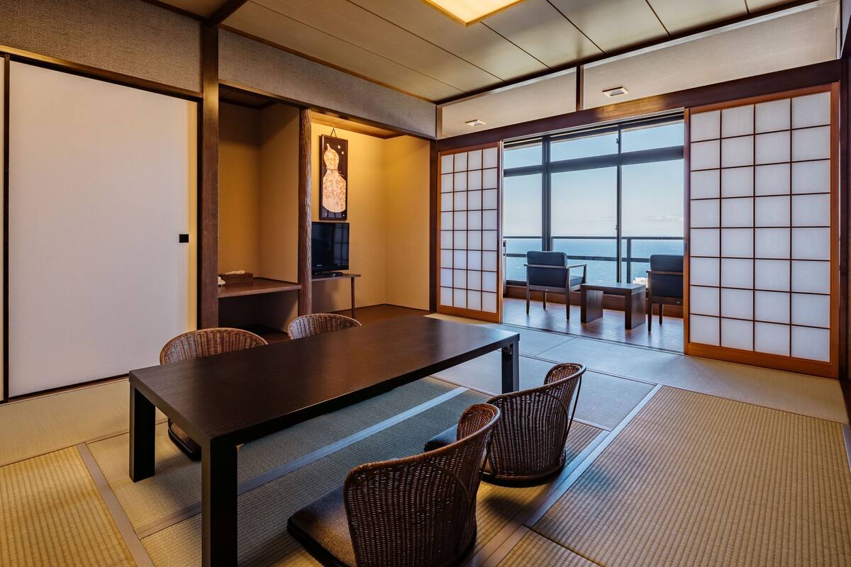 A traditional Japanese room with tatami flooring, a low table, and a view through shoji screens.