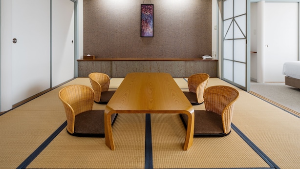 Una habitación tradicional japonesa con suelo de tatami, una mesa de madera baja y sillas tejidas.