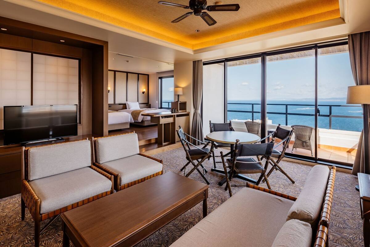 A hotel room with a balcony, a TV, a dining area, and a bed.