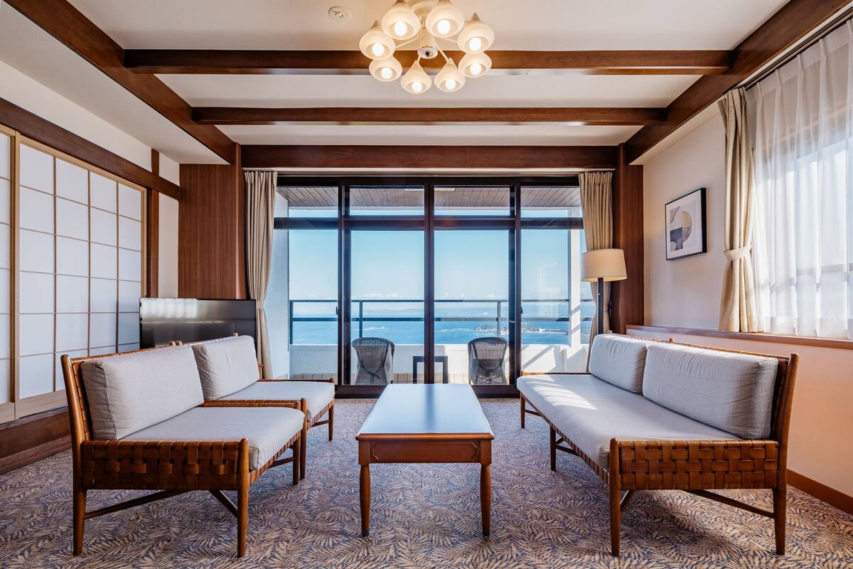 A hotel room with a large window, a sofa, a table, and a television.