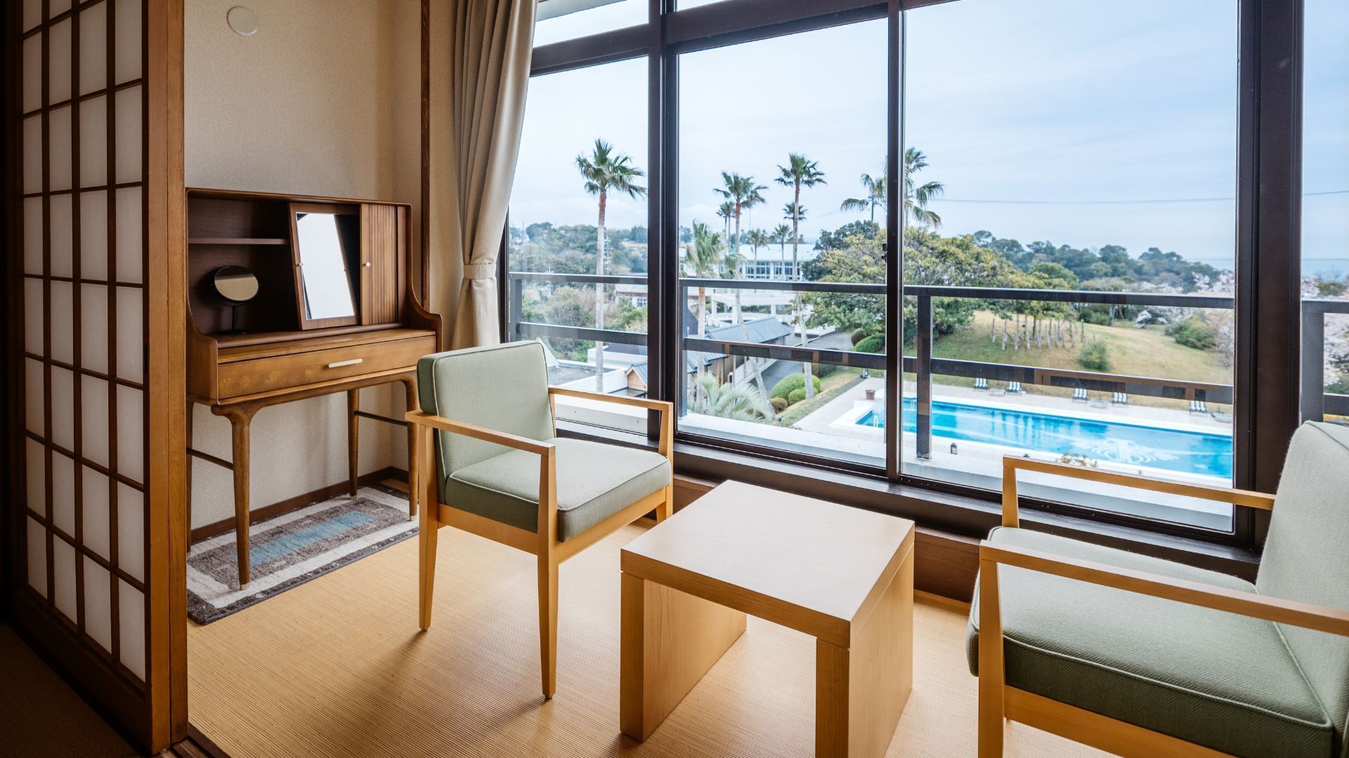 Habitación con vista a una piscina, un escritorio con espejo y dos sillas.