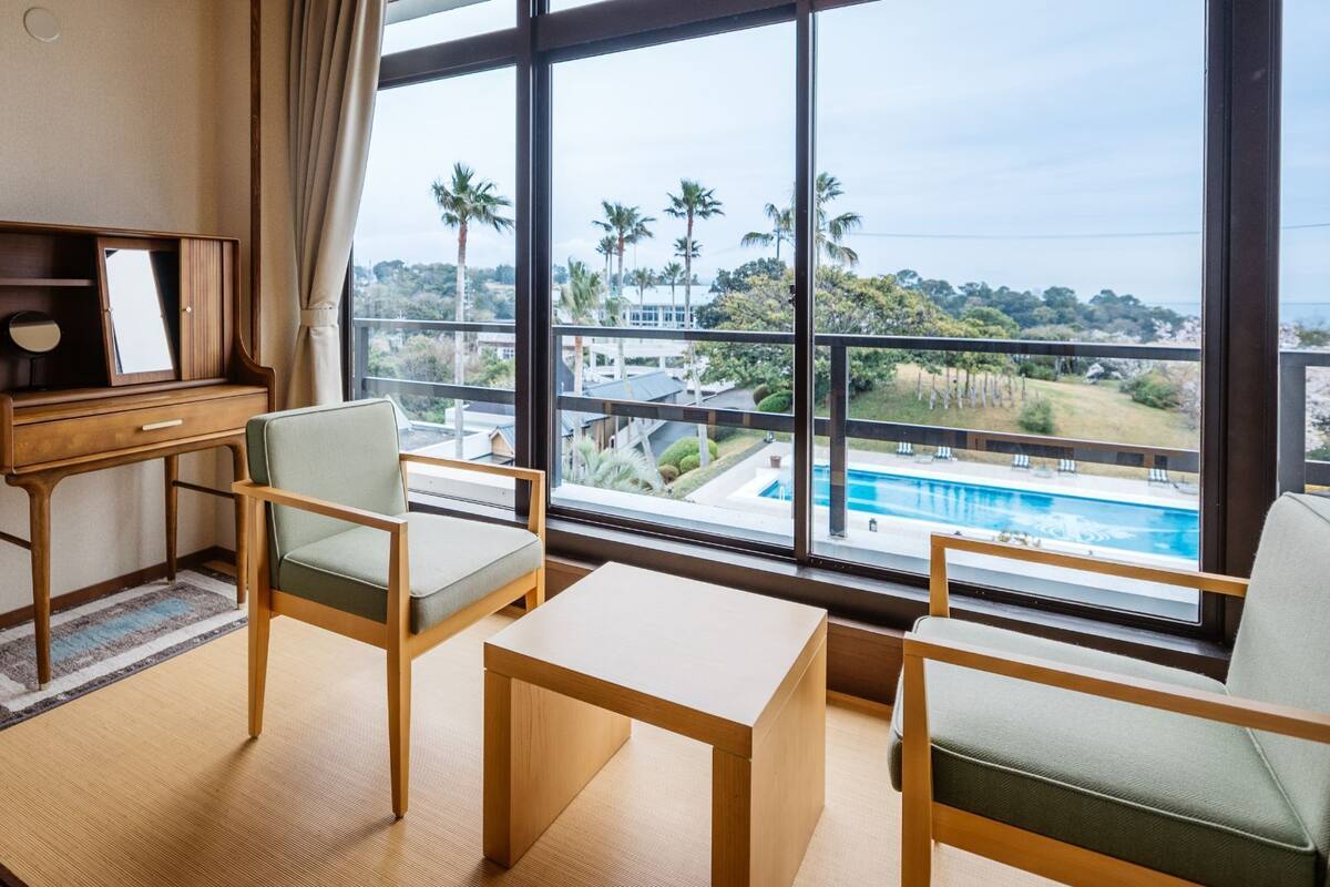 A room with a view of a swimming pool, a desk with a mirror, and two chairs.