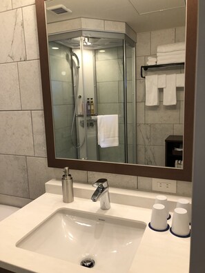 Un baño moderno con un espejo grande, un lavamanos y una ducha con mampara de vidrio.