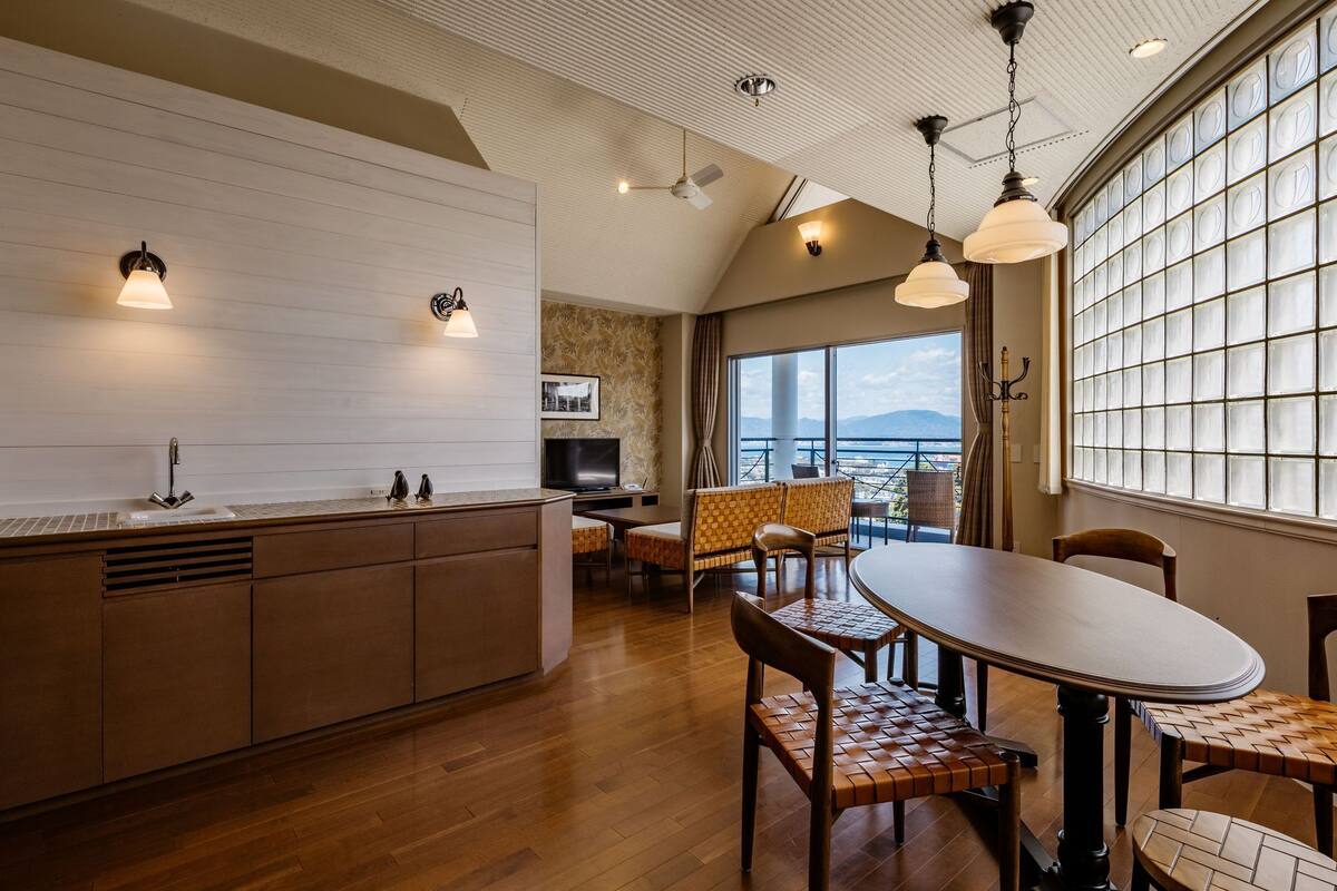 A modern kitchen with a central island, dining area with wooden furniture, and large windows offering a view.