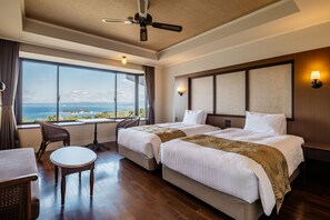 Habitación de hotel con dos camas, una mesa de comedor, una silla, un ventilador de techo y un ventanal con vistas.