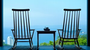 Two rocking chairs facing a table with a ship model, overlooking a scenic view.