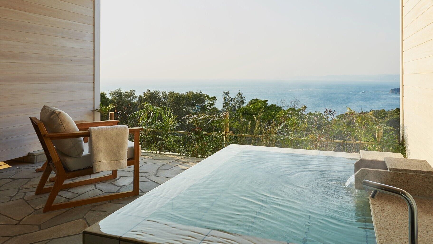 Zona de spa con hidromasaje y una silla, con vista a un paisaje costero.