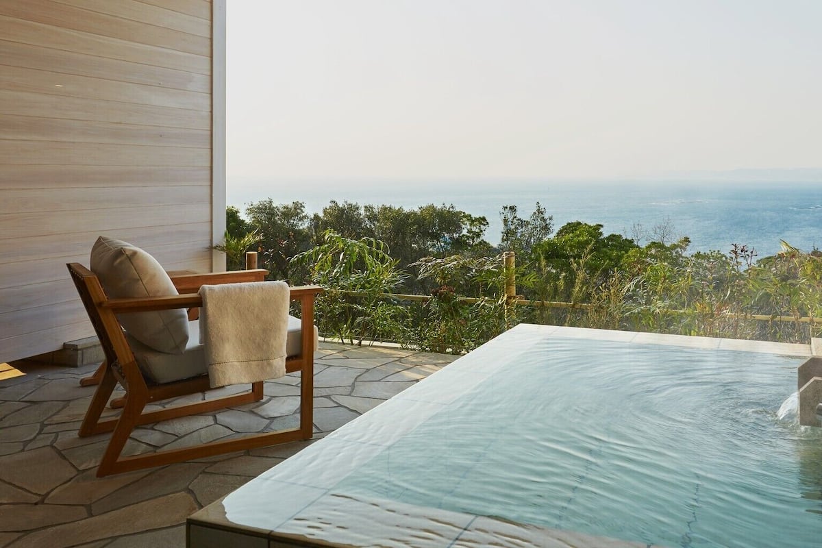 Zona de spa con hidromasaje y una silla, con vista a un paisaje costero.