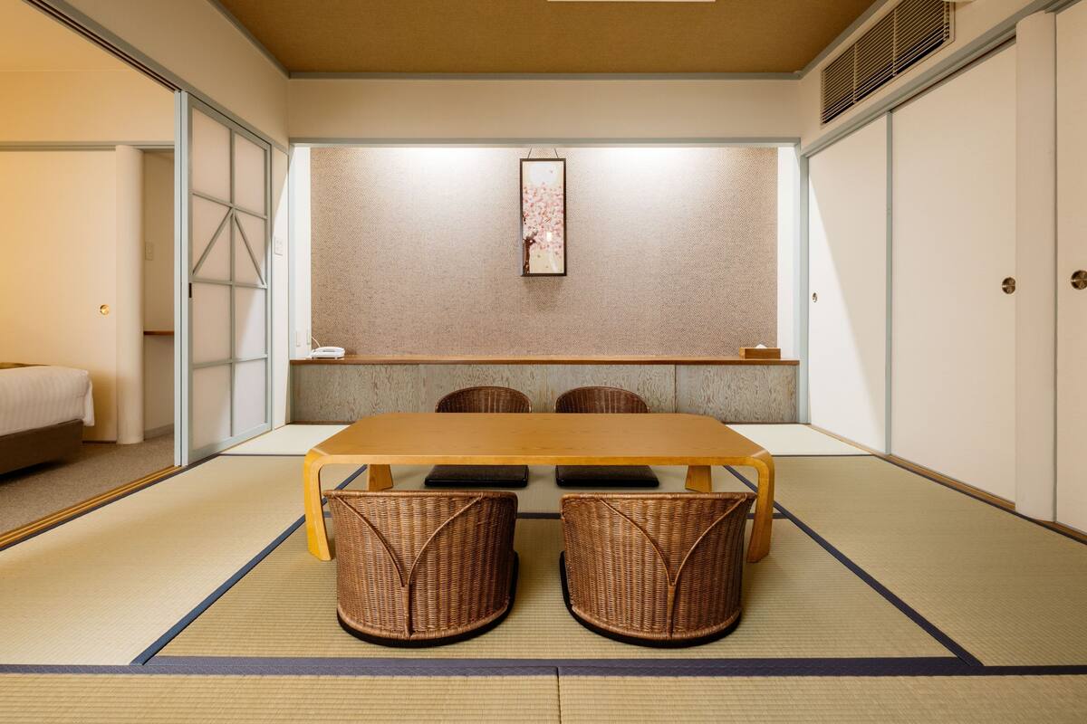 A traditional Japanese-style room with tatami flooring, a low table with four chairs, a bed, and sliding doors.