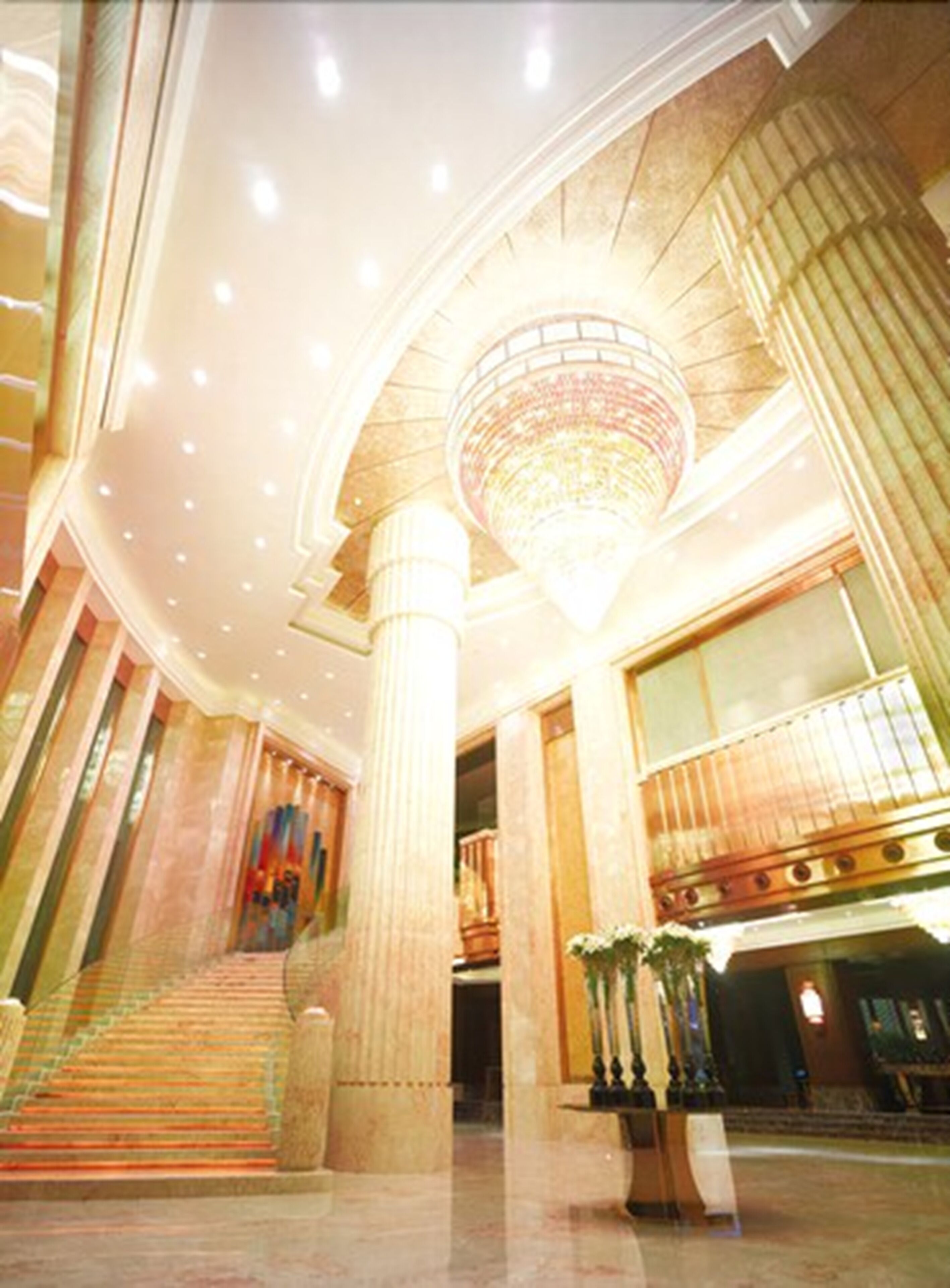 A grand lobby with a large chandelier, marble columns, and a staircase leading to upper floors.