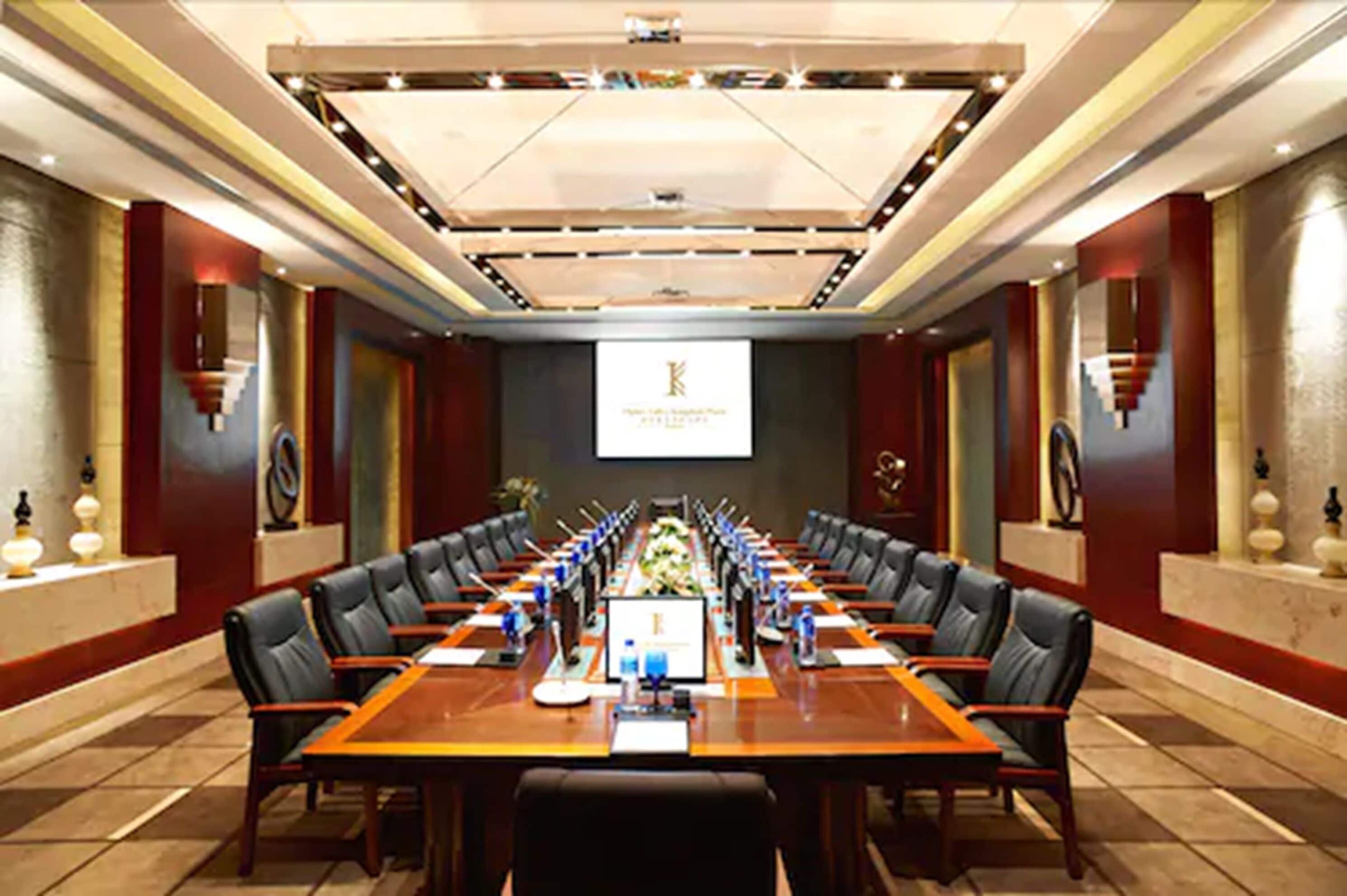 A conference room with a long table, chairs, and a projector screen.