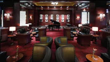 A spacious lounge area with leather seating, a grand piano, and framed pictures on the walls.