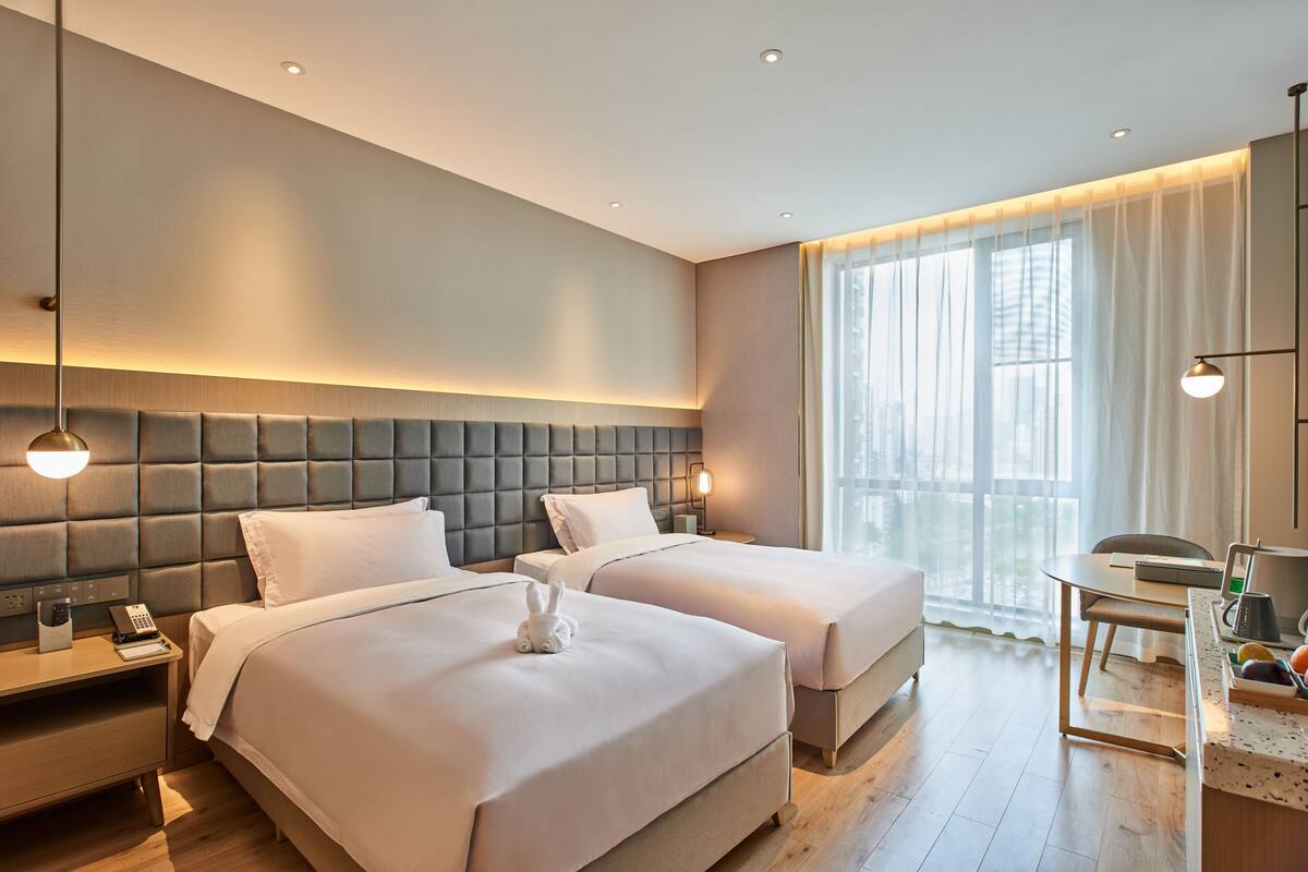 Una habitación de hotel con dos camas, una barra de desayuno y un ventanal con cortinas translúcidas.