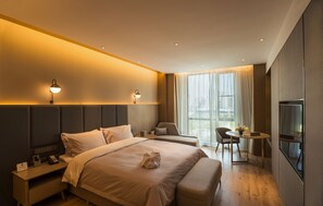 Moderni hotellihuone, jossa on suuri sänky, yöpöydät, työpöytä ja televisio.