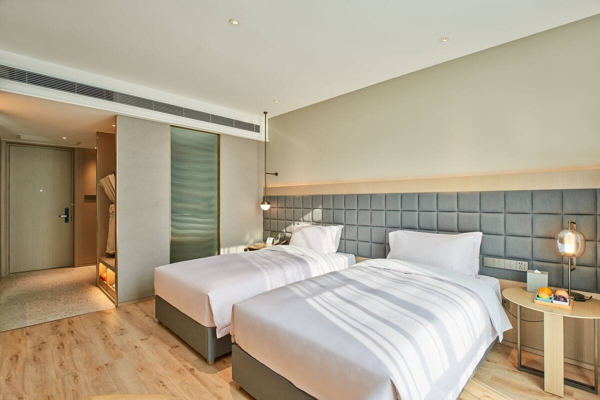 Una habitación de hotel moderna con dos camas, una mesita de noche con lámpara y un armario.