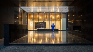 En modern entré med ett reflekterande golv, en blå skulptur och en glasfasad med belysning inuti.