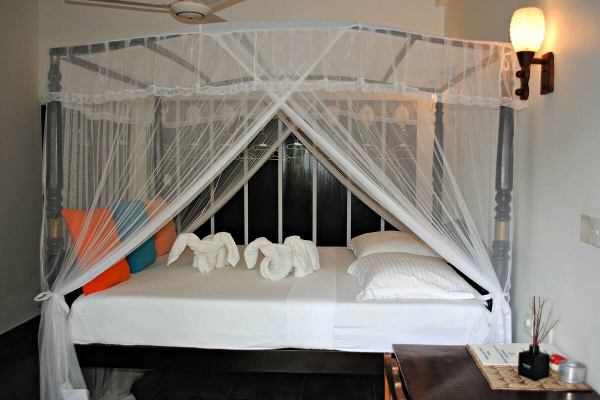 A bed with a canopy, pillows, a bedside table, and a wall-mounted lamp.