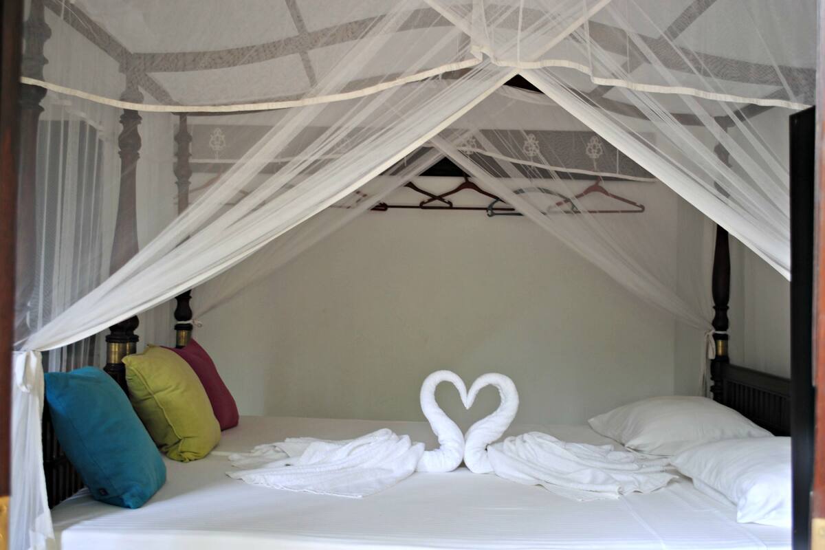 A bed with a canopy, pillows, and a towel arrangement in the shape of swans.