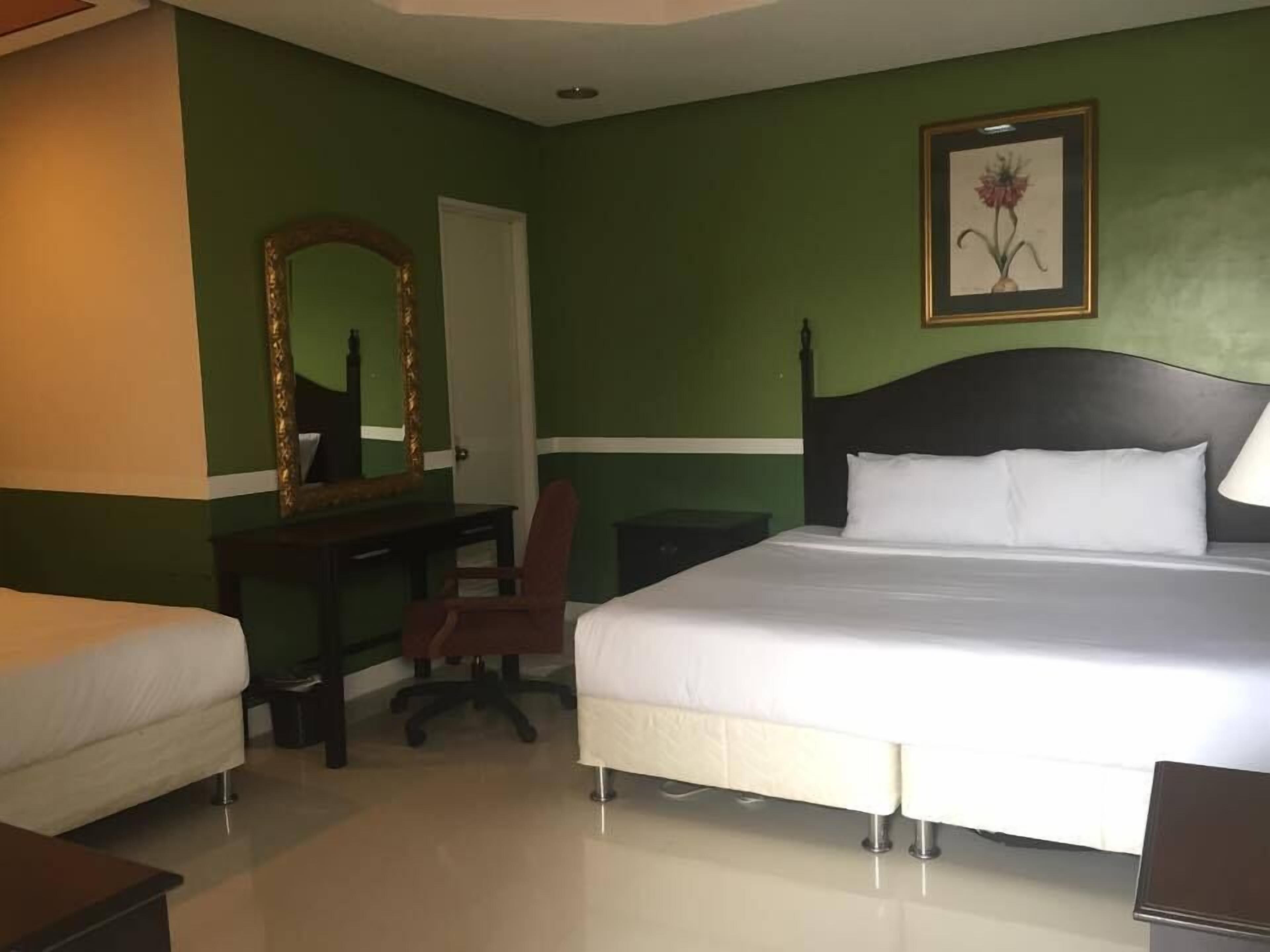 A hotel room with a bed, a desk, a chair, a mirror, and a framed picture on the wall.