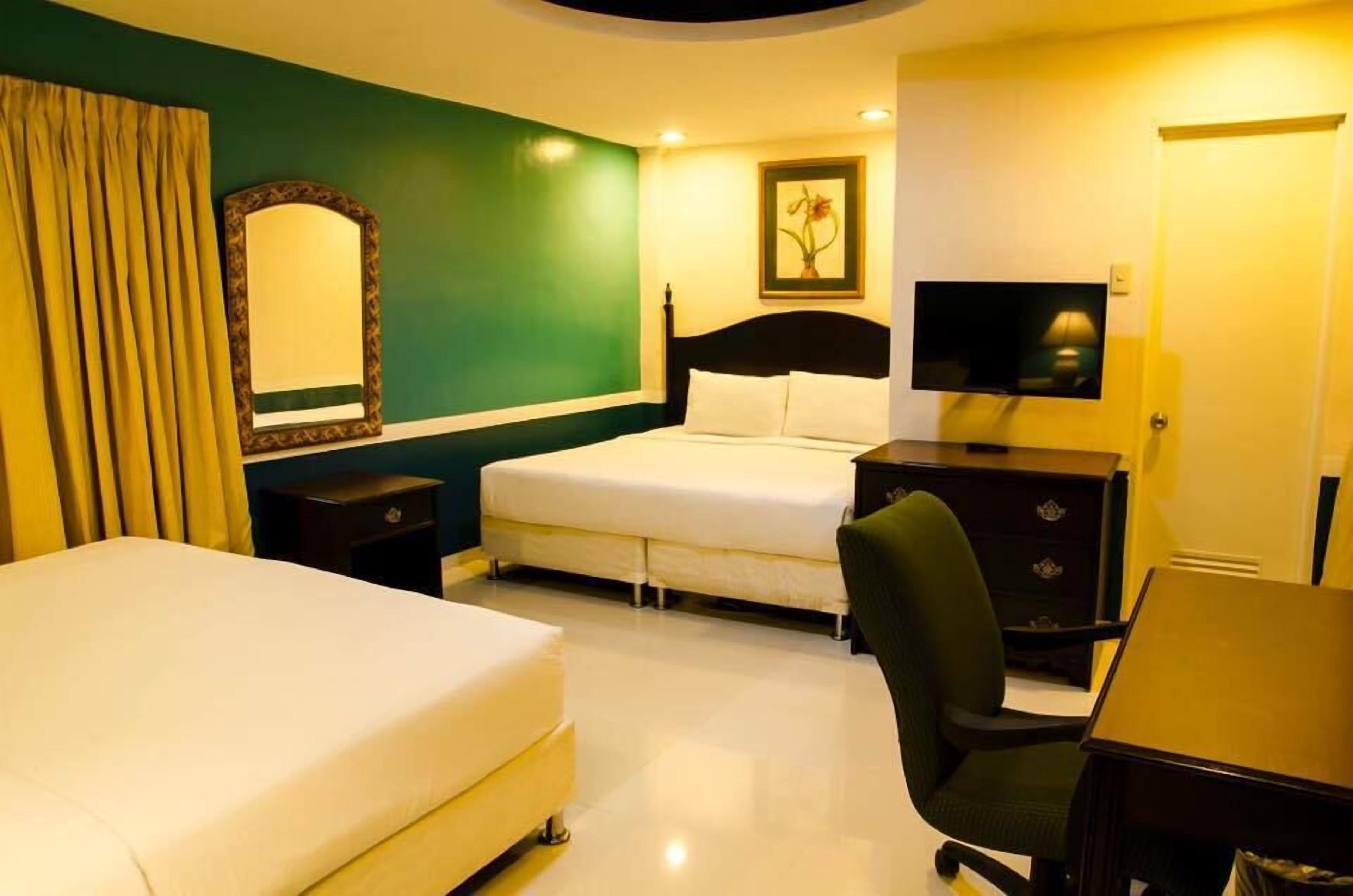 Habitación de hotel con una cama, un escritorio, una silla, un televisor, un aparador y un espejo.