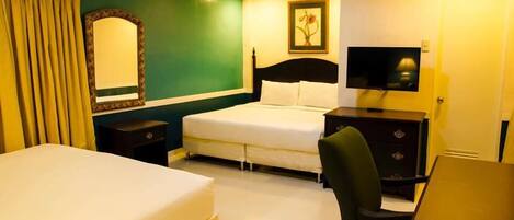 Habitación de hotel con una cama, un escritorio, una silla, un televisor, un aparador y un espejo.