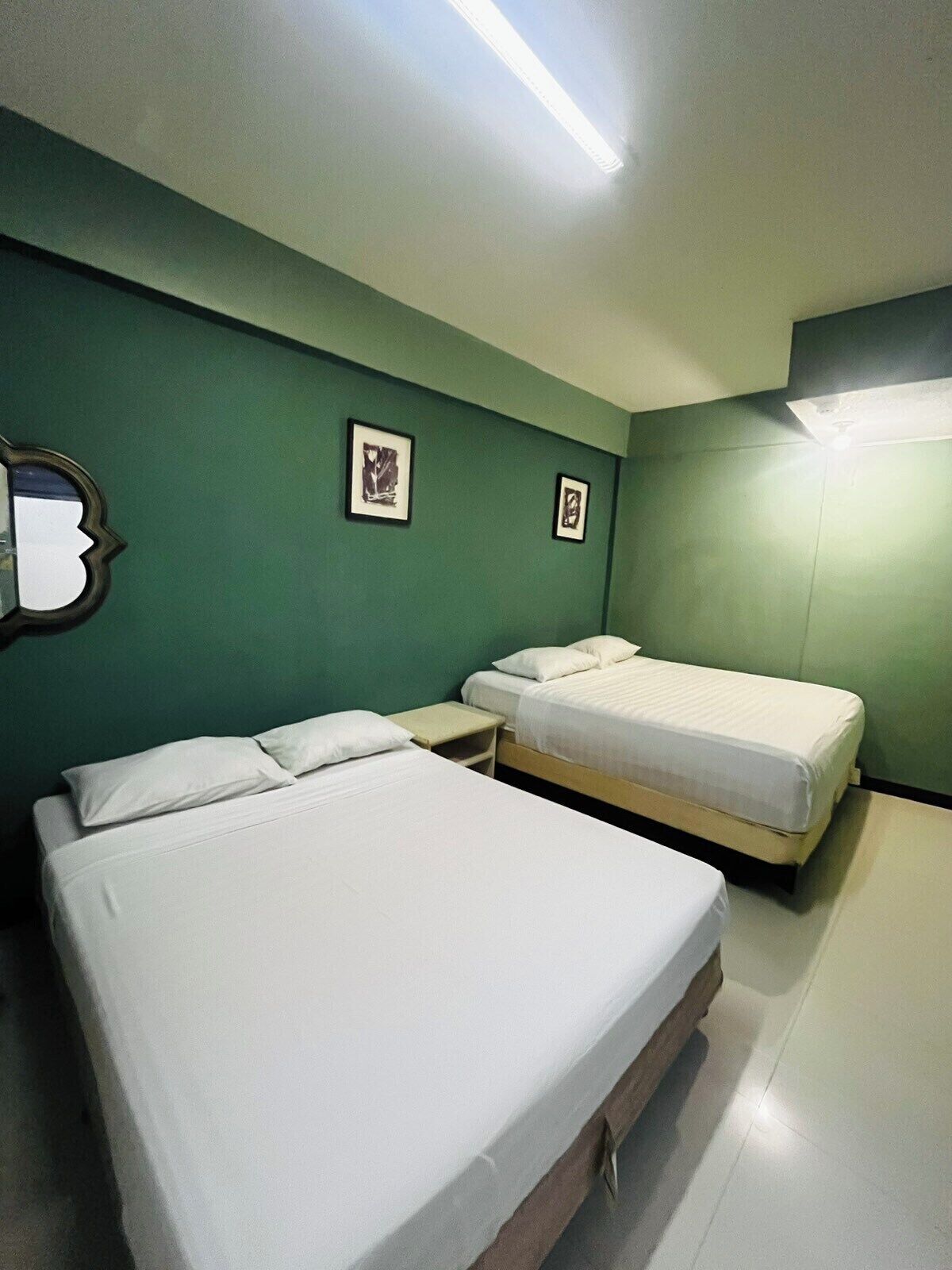 A room with two beds, a small table, and green walls.