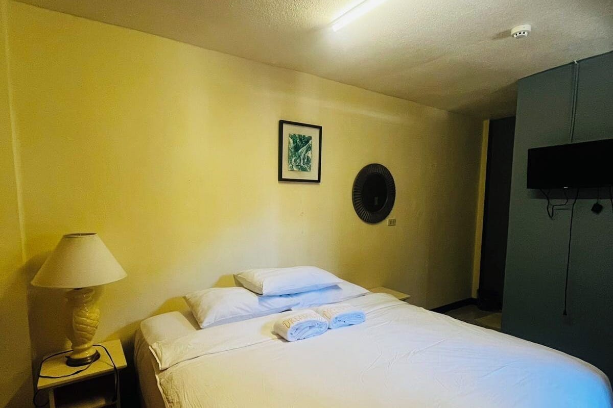 A hotel room with a bed, a nightstand with a lamp, a wall-mounted TV, and a framed picture on the wall.
