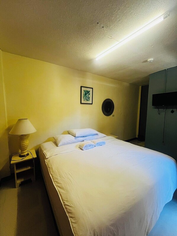 A hotel room with a bed, a nightstand with a lamp, a wall-mounted TV, and a framed picture on the wall. - Dreamwave Resort Pansol (Calamba)