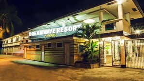 Un hotel llamado "Dreamwave Resort" con un diseño moderno, que presenta un letrero grande, una entrada con portones y una fachada bien iluminada.