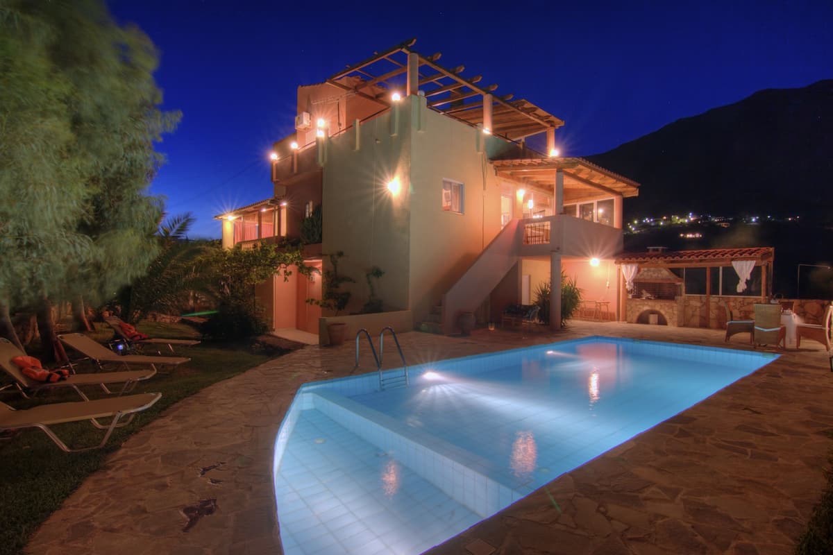 Una piscina con solárium de piedra, sillas de descanso y una escalera que sube a un segundo piso.