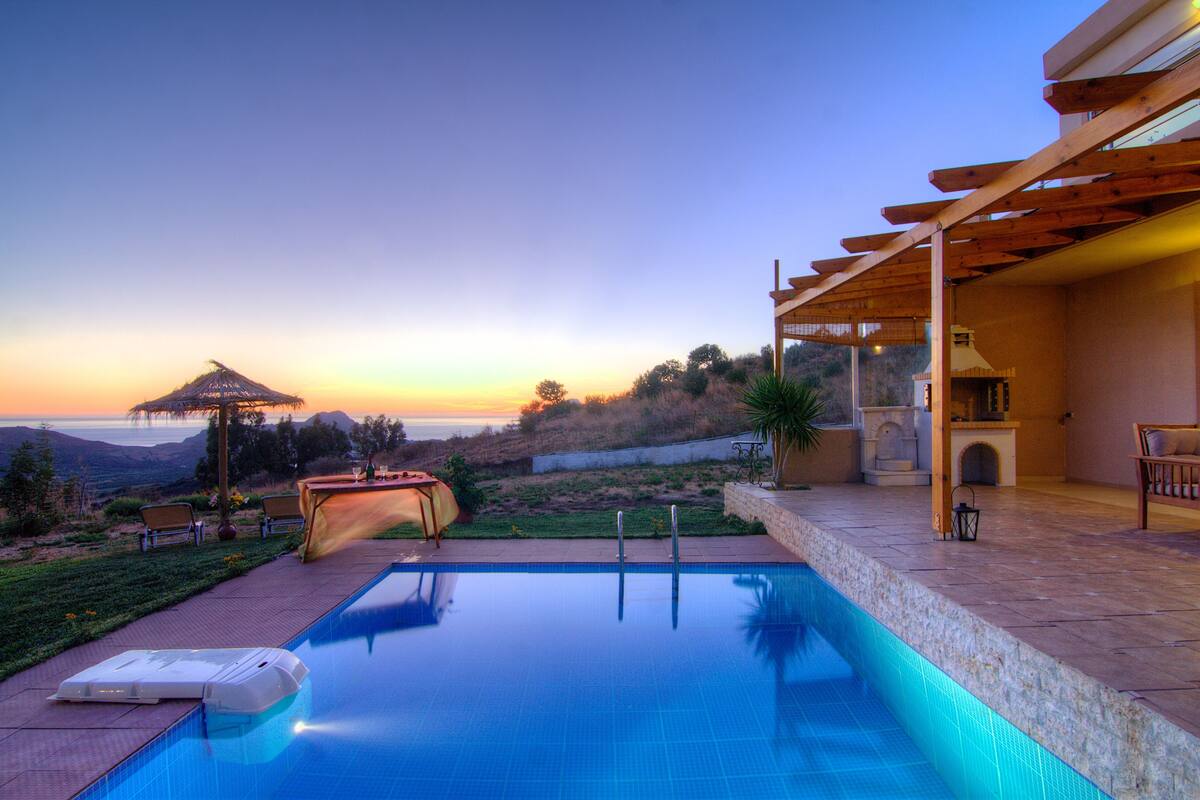 Una piscina con vistas al atardecer, un porche cubierto y mobiliario exterior.